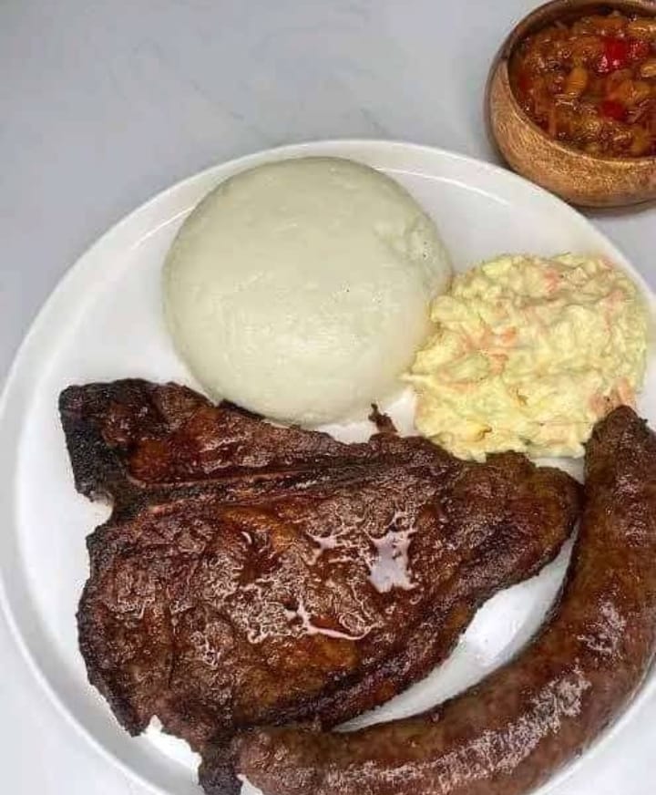 A delicious plate of Nshima with T-Bone steak, sausage, and coleslaw served at Magogo Lodge.